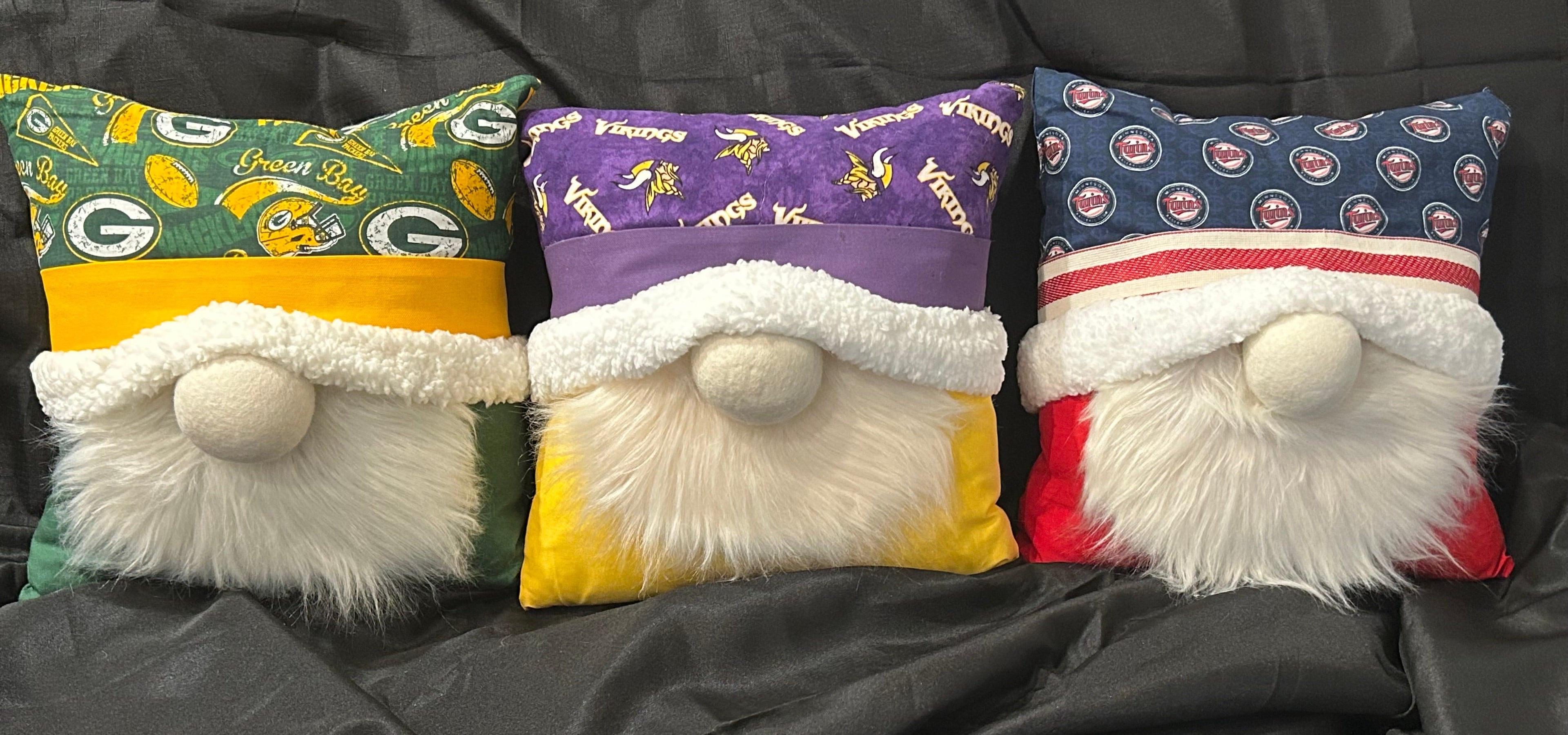 Three gnome-shaped pillows with sports team logos on a bed.